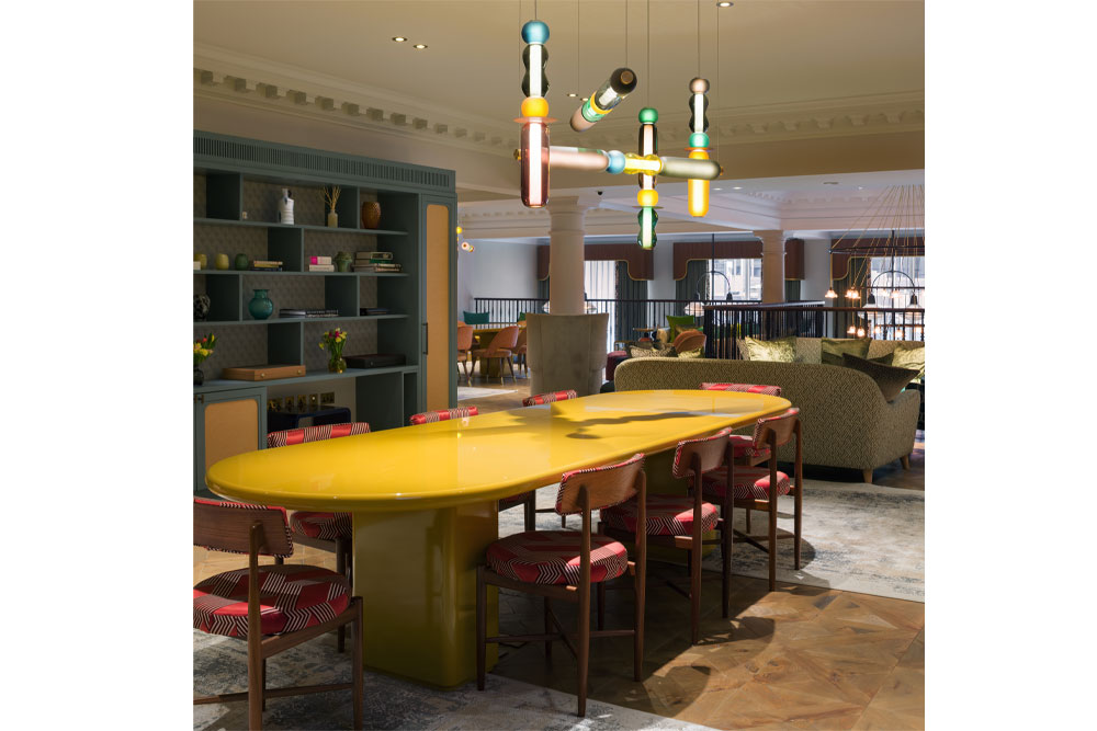 Location photo of the Pavilion Club Knightbridge featuring a sculptural glass beam chandelier hanging over a large contemporary dining table in a yellow lacquer finish.