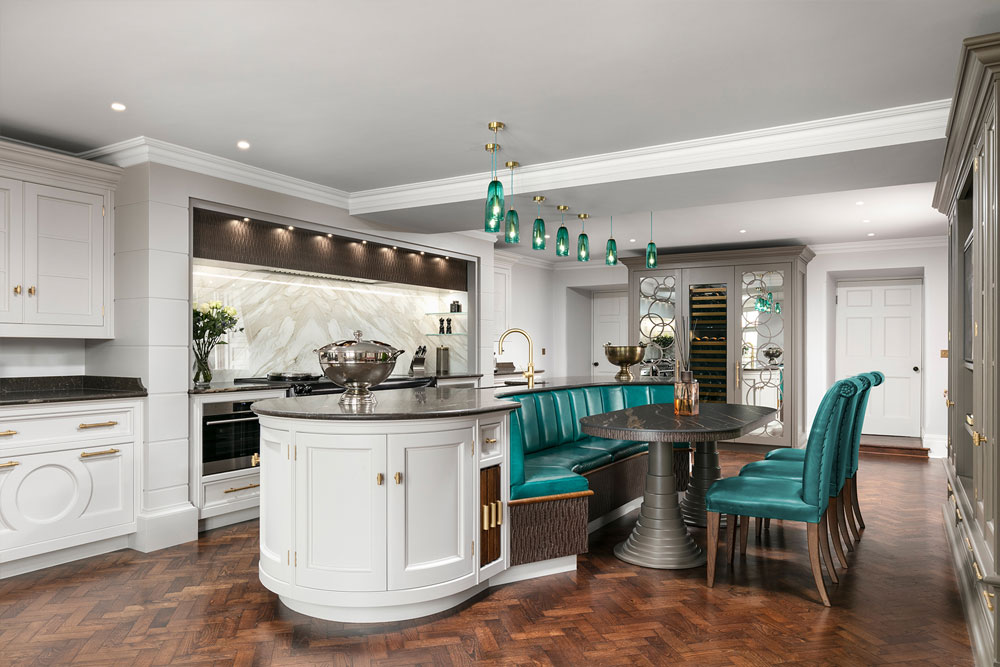 Multiple teal blue hand blown glass pendant lights hanging over a white kitchen island with banquette seating.