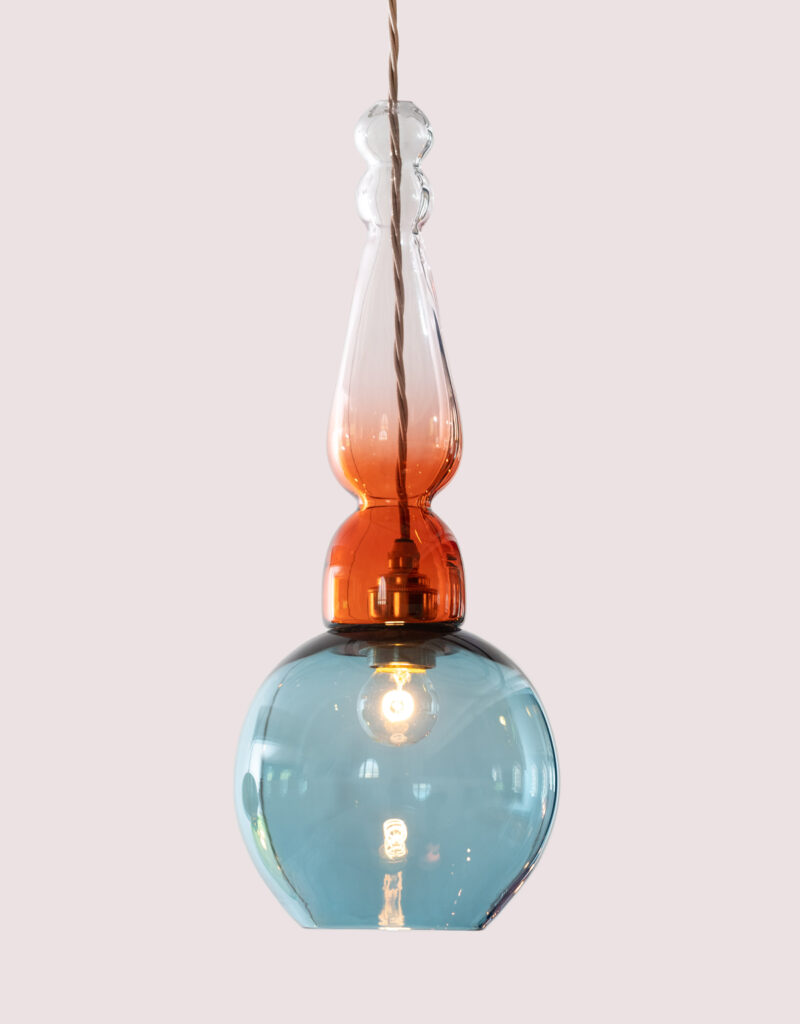 Decorative hand-blown glass pendant light with a round shaped shade in blue and sculptural stem in blush pink.