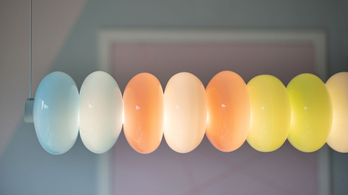 Detailed photo of the Glowbule Bead Beam Pendant Light, a horizontal hanging LED light fixture, which features orbs of hand-blown glass pastel pink, blue, green, and white.