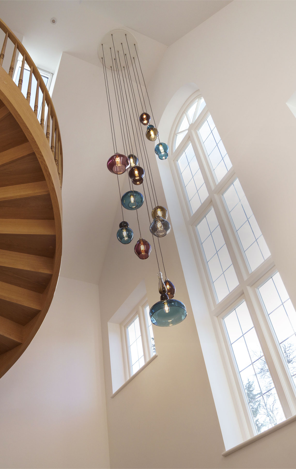Large bespoke glass pendant light chandelier in modern entrance way with high ceiling, featuring glass pendant lights in blue, purple., and olive green.